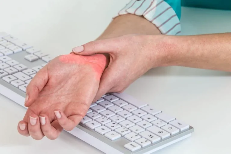 Person holding a painful wrist over a computer keyboard, a common sign of carpal tunnel syndrome