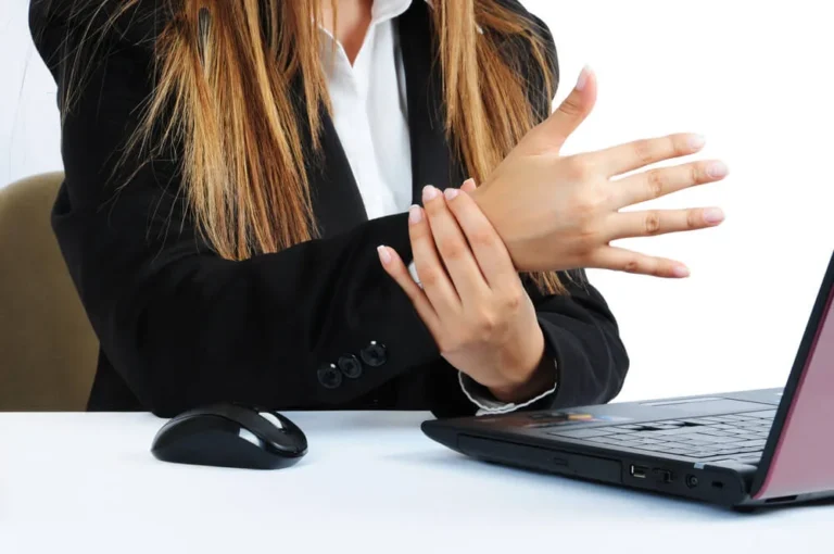 Office worker at a laptop holding her wrist, showing how repeated typing can strain the wrist