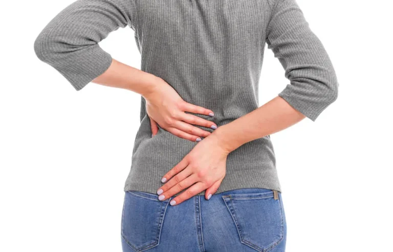 Woman seen from behind holding her lower back with both hands, showing low back pain